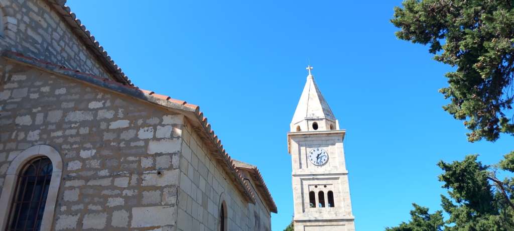 A close-up view of a stone church with a clock tower under a clear blue sky.