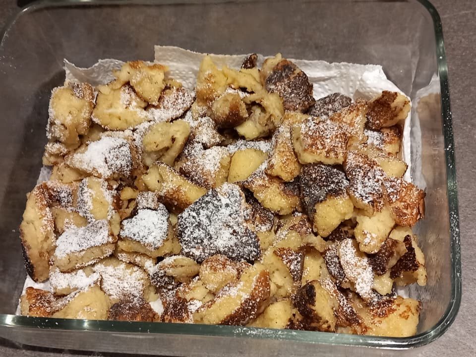 A glass dish filled with small pieces of golden-brown sweet pastry, dusted with powdered sugar.