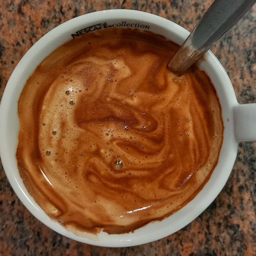 A close-up view of a cup of coffee with a swirling, frothy surface, topped with tiny bubbles, sitting on a textured countertop.