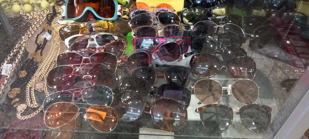 A variety of sunglasses displayed in a glass case, including different styles and colors, alongside some jewelry items.