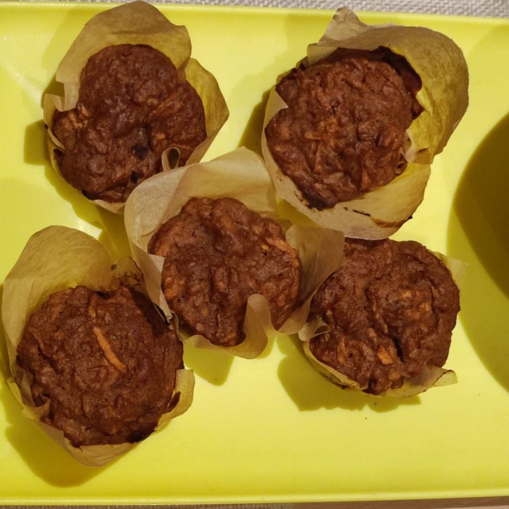 A close-up view of five muffins with a crinkled paper liner, arranged on a bright yellow plate.