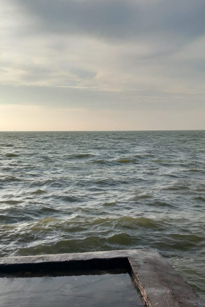 A calm sea under a cloudy sky with a small stone ledge in the foreground.