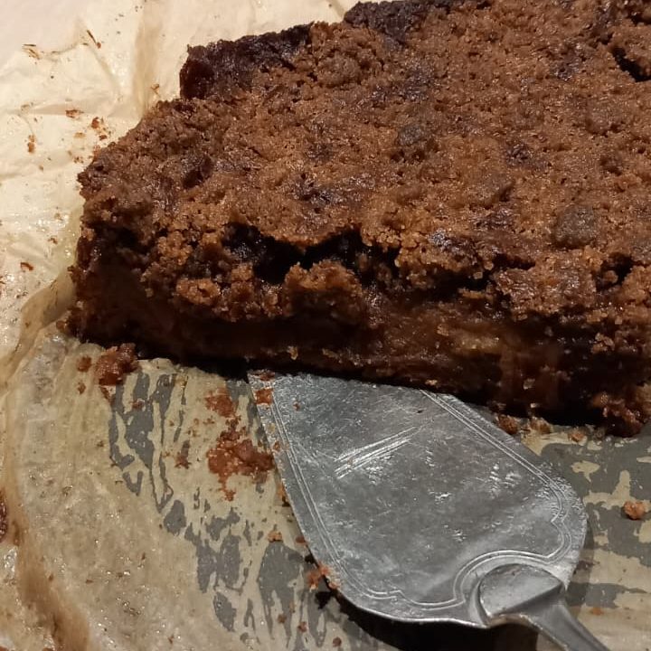 Close-up of a partially cut cake on parchment paper, with a silver serving spatula resting beside it.
