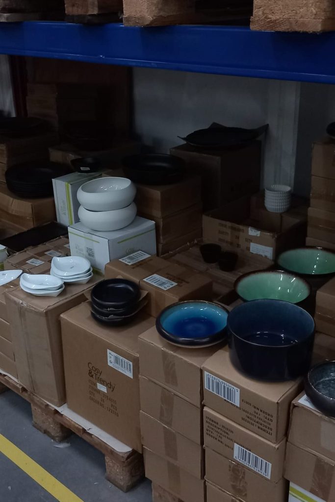 A display of various bowls and plates in different colors on top of cardboard boxes in a storage area.