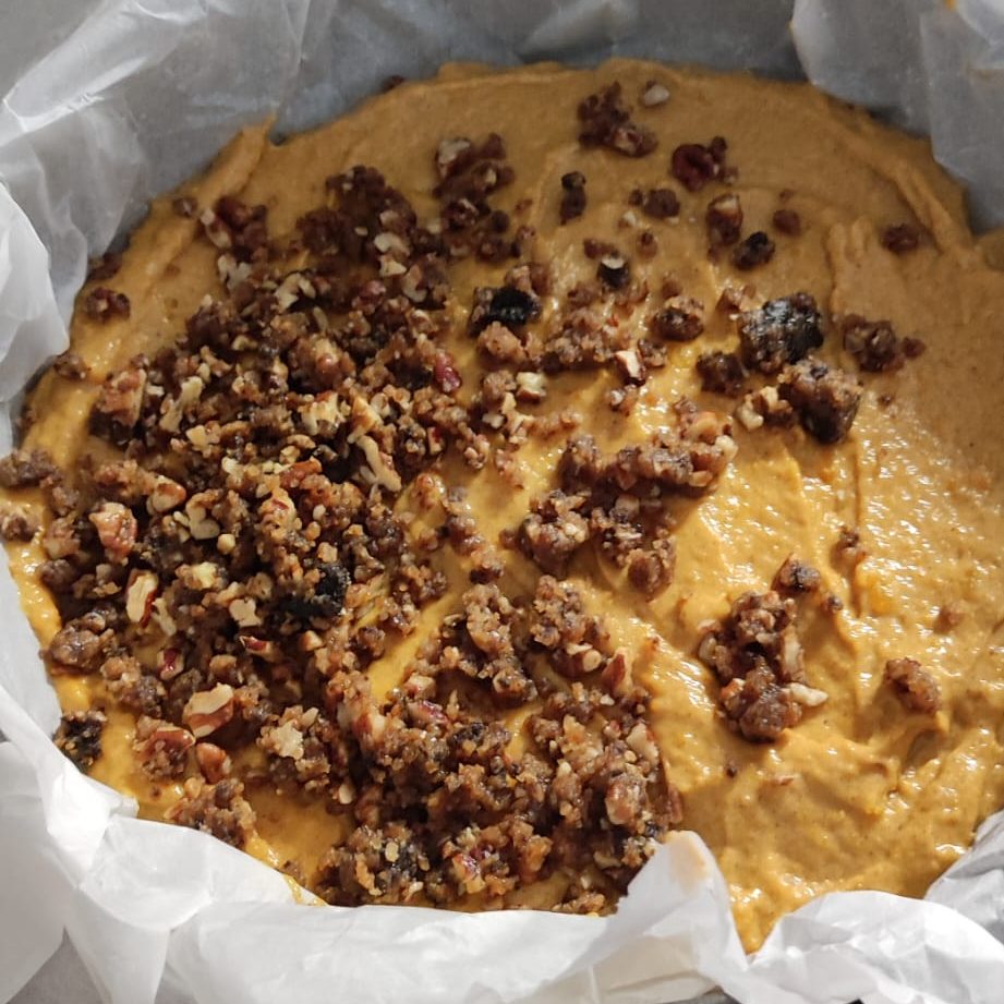 A close-up view of a creamy pumpkin mixture topped with a crunchy pecan streusel, placed in a lined baking dish.