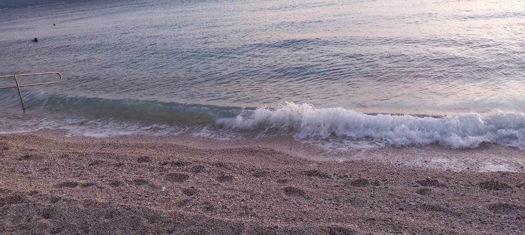 Gentle waves lapping onto a sandy beach with a railing in the background during twilight.