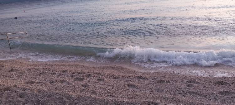 Gentle waves lapping onto a sandy beach with a railing in the background during twilight.
