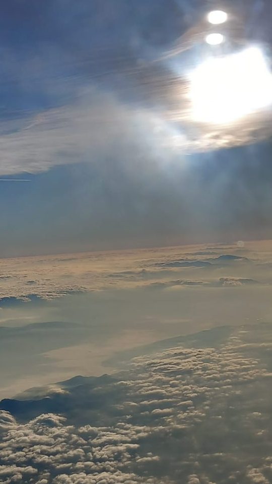 Aerial view of fluffy clouds with a bright sun and a clear blue sky above.