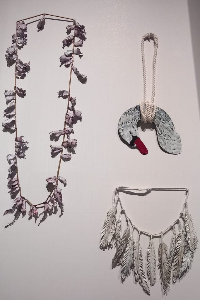 Three decorative wall hangings: a purple leaf garland on the left, a painted swan figure in the center, and a white feather arrangement on the right.