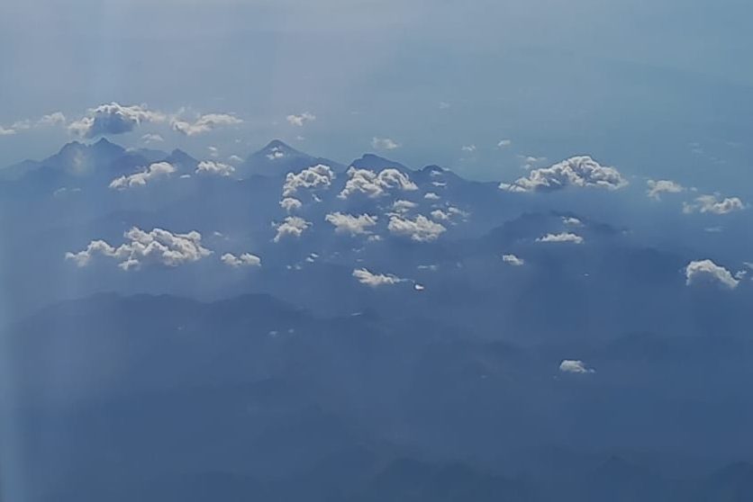 Aerial view of mountainous terrain with clouds scattered above, under a clear blue sky.