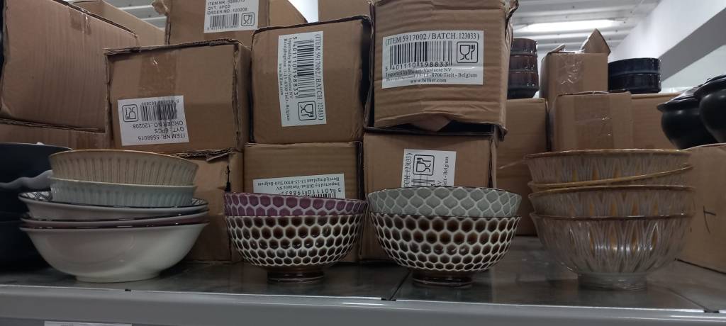 A collection of decorative bowls stacked on a shelf, next to cardboard boxes. The bowls vary in design and color, displaying intricate patterns.